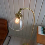 Floor lamp in antique brass finish with clear glass shade and adjustable knuckle joint